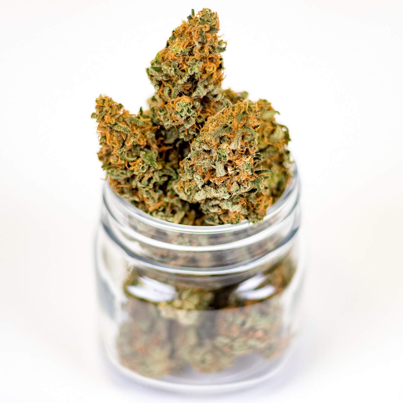 Mason jar with light green marijuana buds, orange hairs, on a white surface.